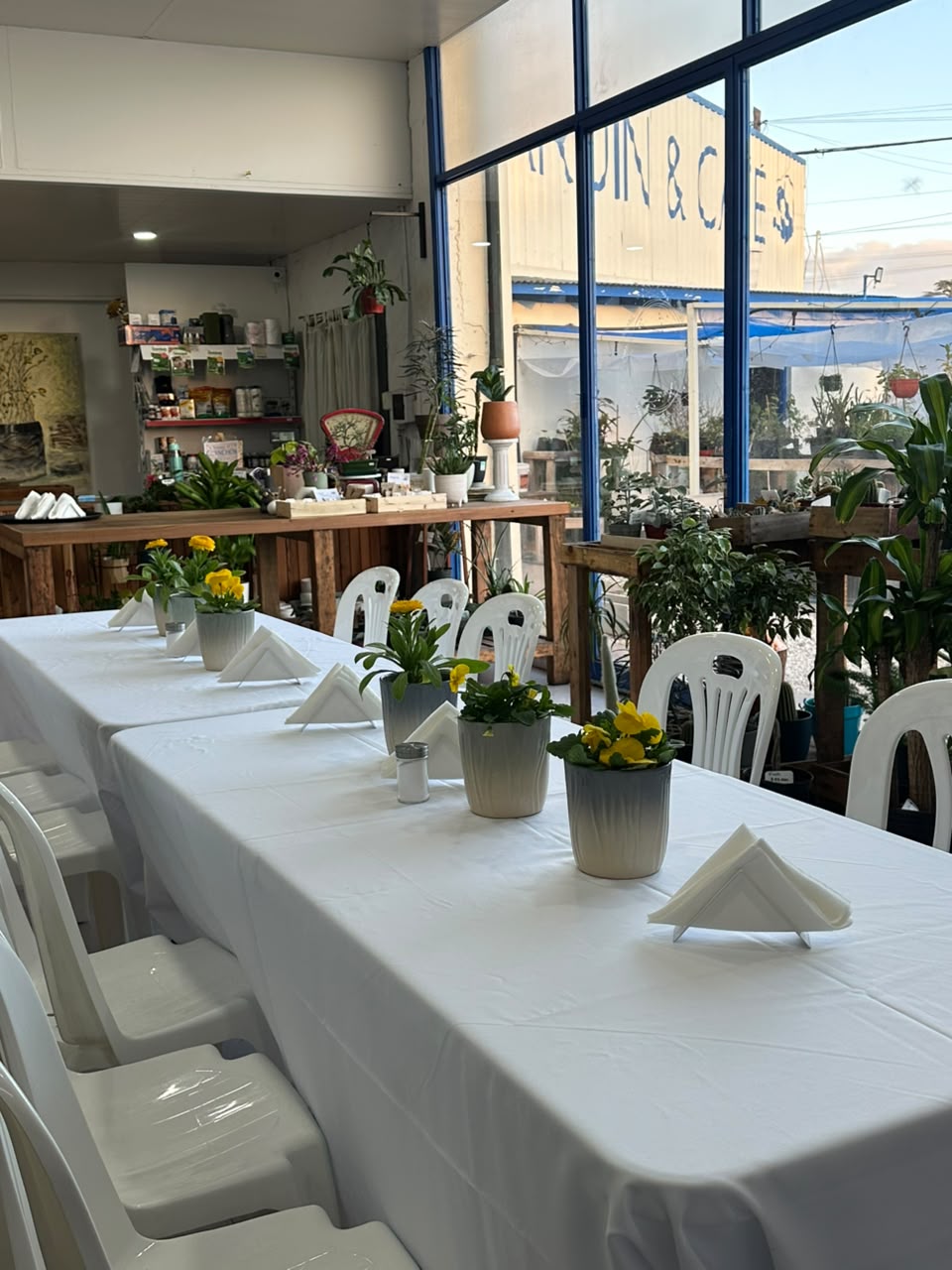 Mesa larga preparada para un evento privado en La Romería, con manteles blancos y plantas con flores amarillas