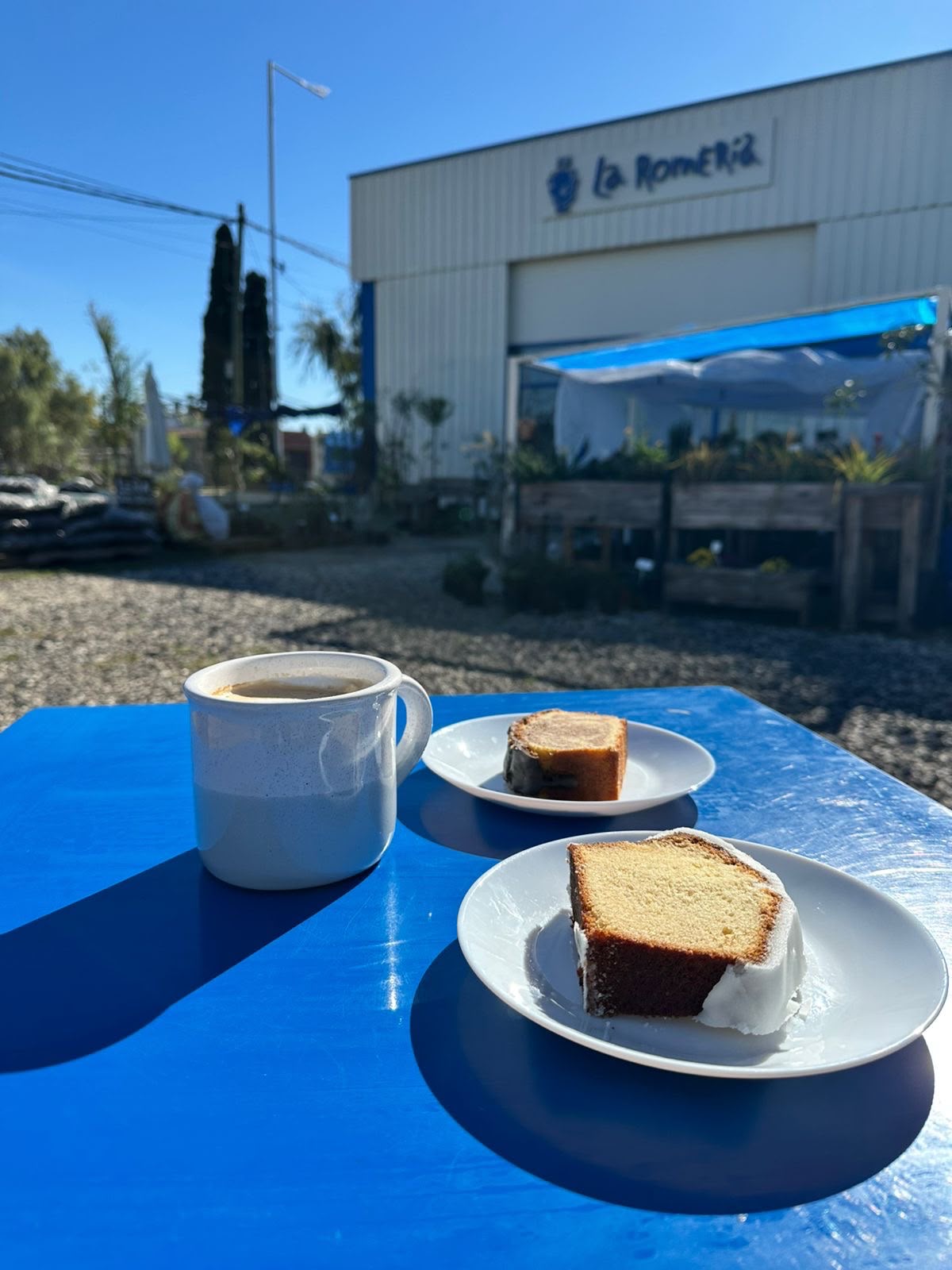 Café y porción de budín en una mesa al aire libre frente al local de La Romería